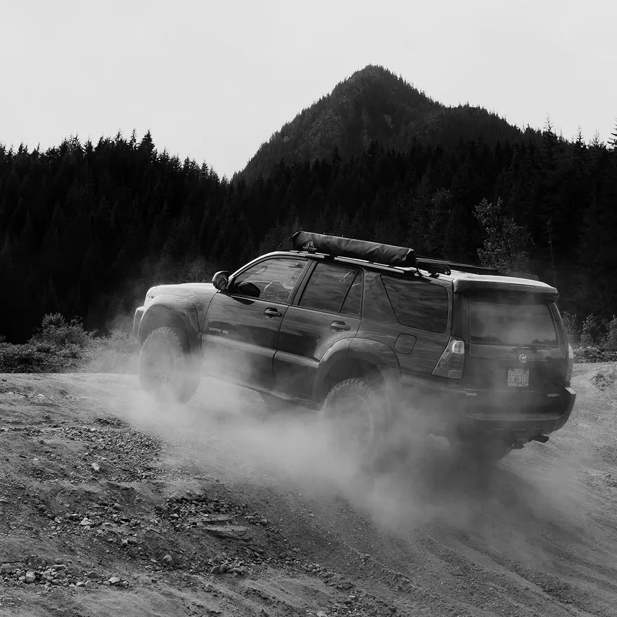 4WD SUV driving on dusty gravel road in mountainous terrain, showing heavy dirt buildup suited for Tasman Autowash off-road vehicle cleaning